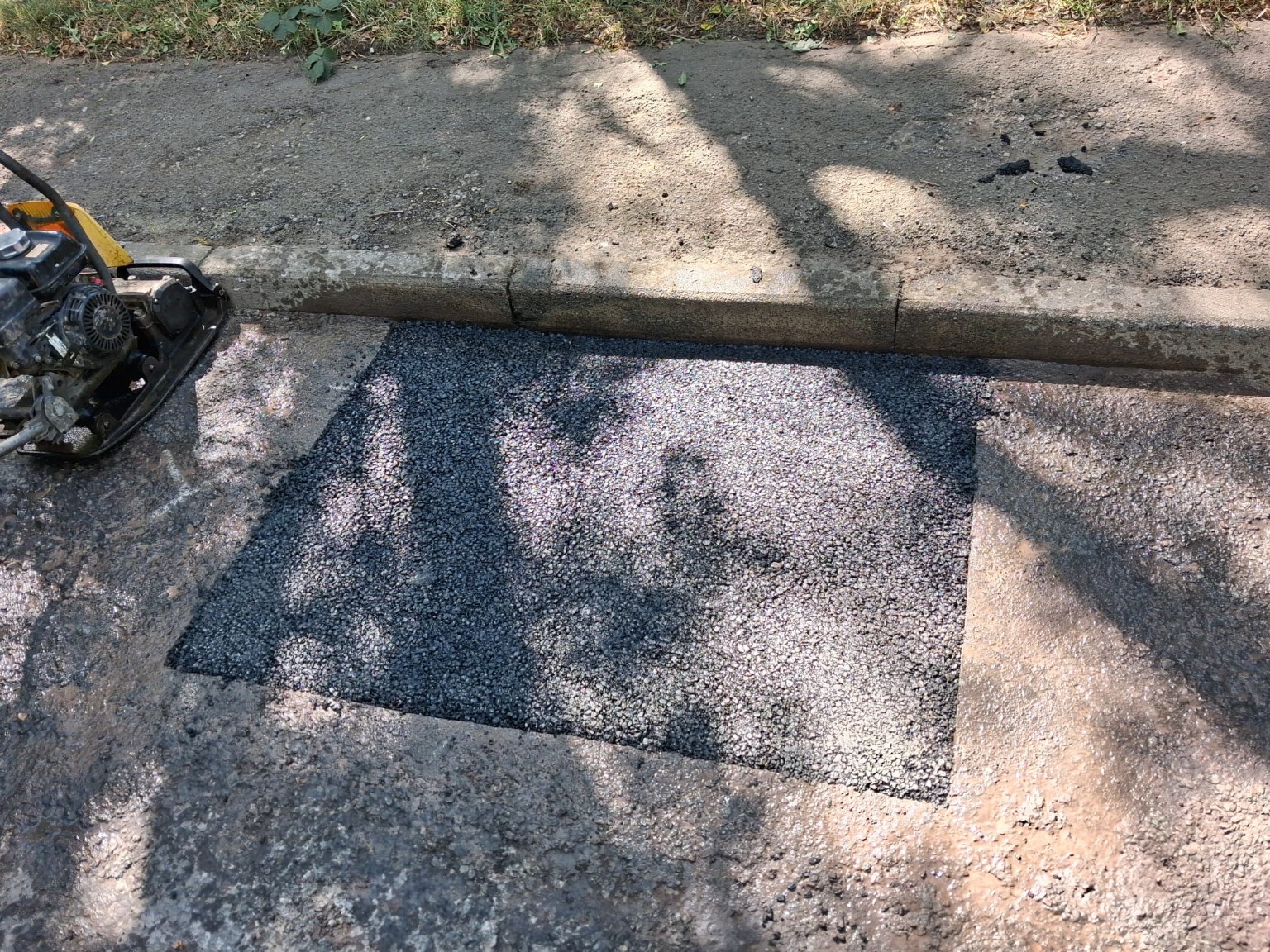 Outdoor Restore tarmac patch repair beside a kerb, with a plate compactor alongside